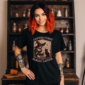 May include: Black t-shirt with a vintage-style illustration of a witch reading a book with a black cat. The text "Coffee First Magic Later" is printed on the shirt.