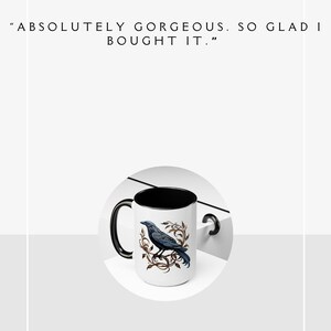 May include: A white ceramic mug with a black rim and handle. The mug features a black raven perched on a branch with brown and gold leaves. The text "ABSOLUTELY GORGEOUS. SO GLAD I BOUGHT IT." is below the image. The mug is on a white surface.  "ROBIN 8/31/24" is below the mug.