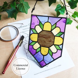 May include: A stained glass sunflower with yellow, green, purple, and blue glass pieces. The sunflower is framed in black and has a hanging cord. The image also shows a pattern for the stained glass project, a glass cutter, and copper tape.