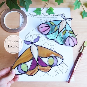 Può includere: Un progetto artigianale di vetrate a forma di falena con una combinazione di colori rosa, blu e giallo. L'immagine include un rotolo di lamina di rame, un tagliavetro e un foglio modello etichettato "Magic Moth Bundle".