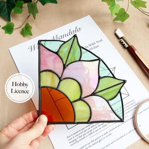 May include: A stained glass mandala in a corner design, featuring pink, green, yellow, and orange hues. The artwork is framed with black lines and includes the text "Hobby Licence" on a white circle. The design is on a white paper with text.