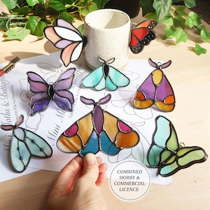 May include: A selection of stained glass moths and butterflies in vibrant colours. The insects are displayed in shades of purple, orange, and teal. Some are attached to a ceramic mug. The image also includes a sheet of paper with the text "Mini Moths & Butterflies".
