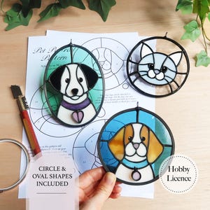 Op de afbeelding: Drie glas-in-lood portretten van huisdieren: een hond in een ovale lijst, een kat in een ronde lijst en een hond in een ronde lijst. De hondenportretten hebben zwart-witte en bruin-witte kleuren. Het kattenportret is lichtblauw en wit. De tekst "CIRCLE & OVAL SHAPES INCLUDED" is zichtbaar.