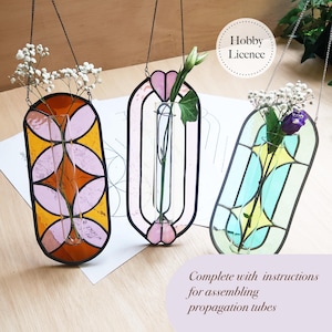 May include: Three stained glass propagation tubes in orange, pink, and teal, each with a different floral arrangement. The tubes are suspended by chains. The text "Hobby Licence" is in a circle, and the text "Complete with instructions for assembling propagation tubes" is below.