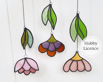 May include: Five stained glass flower and leaf ornaments hanging from black chains. The flowers are pink, orange, and purple with green leaves. The ornaments are on a white background.