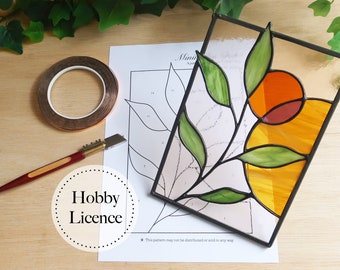 May include: A stained glass project featuring a floral design with green leaves and orange, yellow, and red glass pieces. The project is on a white paper with a black and white pattern and the text "Hobby Licence".