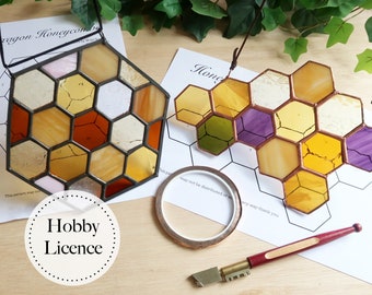 May include: Two stained glass honeycomb panels, one with purple and green accents, the other with orange and brown accents, on a wooden surface with a printed pattern, copper tape, a glass cutter, and a hobby licence.