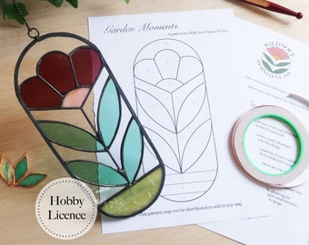 May include: A stained glass pattern for a flower with green leaves and a red centre. The pattern is printed on white paper with the title "Garden Moments" and the text "This pattern may not be distributed or sold in any way".