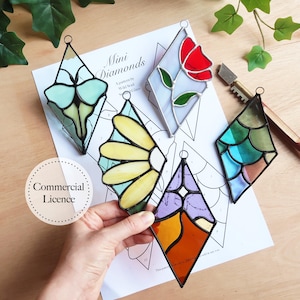 May include: Five stained glass diamond-shaped ornaments with a variety of designs, including a butterfly, a flower, a tulip, a seashell pattern, and a geometric design. The ornaments are displayed on a white sheet of paper with a black and white pattern and the text "Mini Diamonds A pattern by Wild Stained Glass"