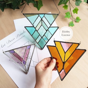 May include: Three triangular Art Deco stained glass panels. One is turquoise, another is orange and pink, and the third is purple and pink. Each panel has a metal frame and a chain for hanging. The text "Art Deco Panels" is visible.