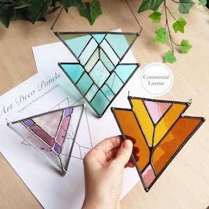 Op de afbeelding: Drie Art Deco glas-in-lood panelen in driehoekige vormen. Eén is turquoise en wit, een andere paars en roze, en de derde oranje en roze. Elk paneel heeft een metalen frame en een ketting om op te hangen.