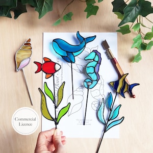 以下が含まれることがあります： カラフルなステンドグラスの海の生き物と植物のステークスのコレクション。ステークスには、貝殻、赤い魚、青いクジラ、タツノオトシゴ、黄色と青の魚、緑と青の植物が含まれます。画像にはツールとテキスト「Commercial Licence」も含まれています。