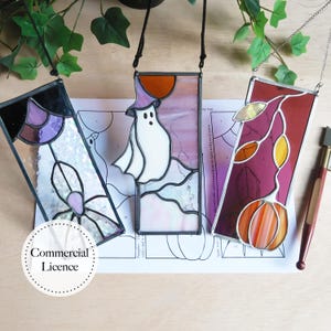 May include: Three stained glass panels with Halloween themes. The panels are rectangular and feature a ghost, a pumpkin, and a leaf design. The panels are made with iridescent glass and have black metal frames.