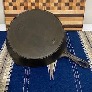 May include: A cast iron skillet with a black finish. The skillet has a handle with a loop at the end. The bottom of the skillet is marked with "Wagner Ware Stoney Co."
