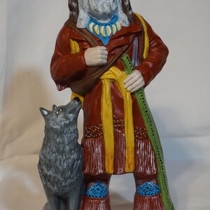 May include: A hand-painted ceramic figurine of a man wearing a red and yellow robe with a fur-trimmed hat and holding a staff. He is standing next to a gray wolf.