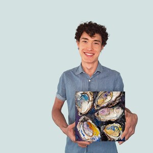 May include: A man is holding a painting of a group of oysters. The oysters are painted in a variety of colors, including purple, blue, yellow, and white. The painting is on a dark background.