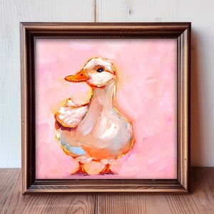Op de afbeelding: Een ingelijst schilderij van een witte eend met een oranje snavel op een roze achtergrond. De eend is geschilderd in een losse, impressionistische stijl.