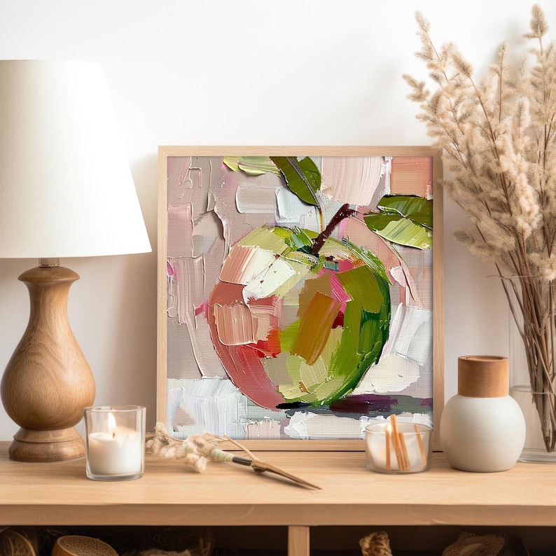 May include: A framed painting of a single green apple with pink and yellow highlights, painted in a loose, impressionistic style. The apple is on a white background with a light pink and gray background.