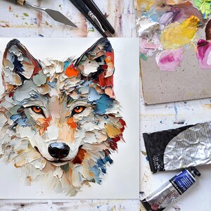 May include: A colorful oil painting of a wolf's head. The artwork features textured brushstrokes in shades of white, blue, orange, and red. The wolf has orange eyes and a black nose. Art supplies, including paint tubes and a palette, are visible.