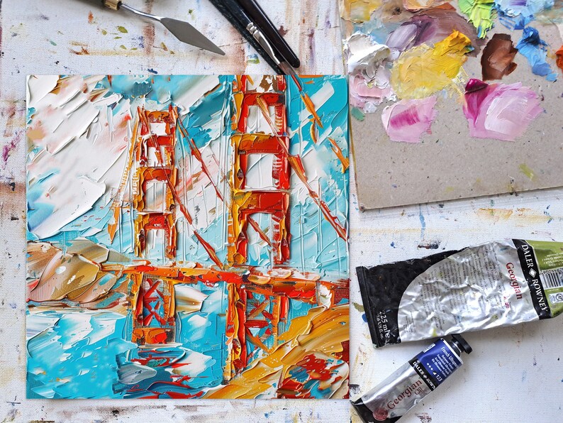 May include: A close-up of a painting depicting the Golden Gate Bridge in San Francisco. The painting is executed in a thick, impasto style using vibrant colours of red, orange, yellow, blue and white.
