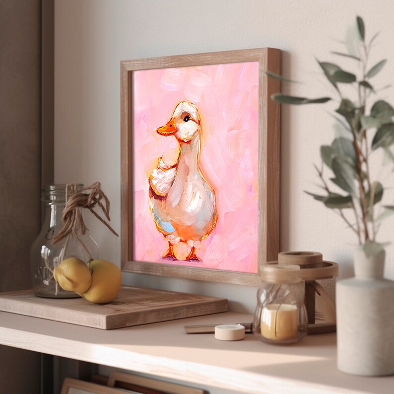 Op de afbeelding: Een ingelijst schilderij van een witte eend met een oranje snavel die op een roze achtergrond staat.