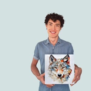 May include: Square canvas art featuring a colorful, textured painting of a wolf's face. The artwork uses a palette of blues, oranges, and whites. The painting is held by a person wearing a blue denim shirt.