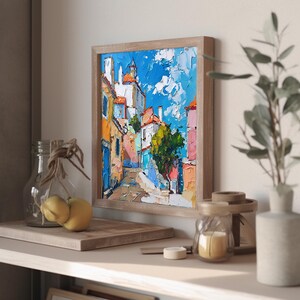 May include: A framed painting of a colorful cityscape with a blue sky and white clouds. The buildings are painted in a variety of colors, including yellow, orange, pink, and blue. The painting is in a wooden frame.