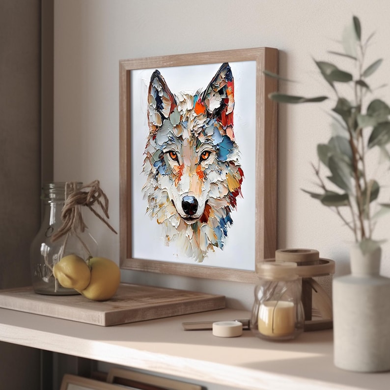 May include: A framed art print featuring a colorful, textured painting of a wolf's head. The artwork uses a palette of white, orange, blue, and red. The framed print is displayed on a shelf with decorative items, including a glass jar and a small candle.