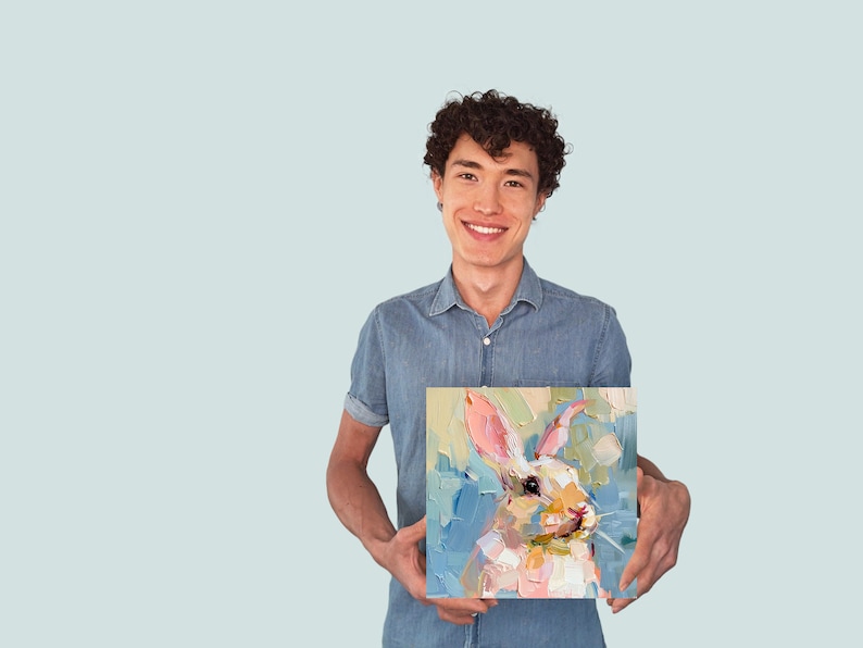 May include: A person holding a painting of a white rabbit with pink ears and a blue background. The rabbit is painted in a loose, impressionistic style.