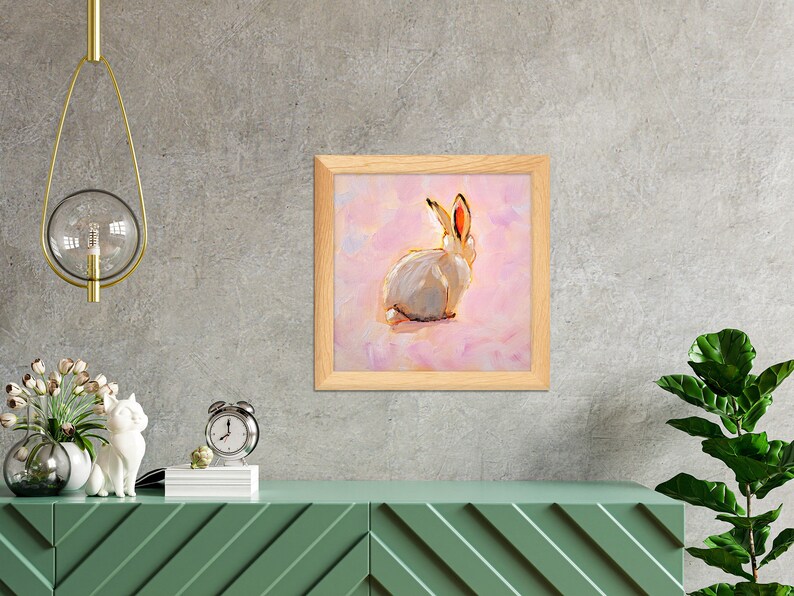 May include: A framed painting of a white rabbit with pink ears sitting on a pink background.