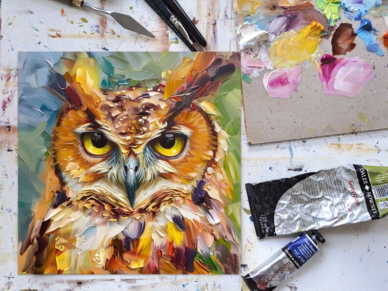 May include: A close-up painting of an owl with yellow eyes. The owl is painted in a colorful, abstract style with a variety of brushstrokes. The background is a blurred green and blue.