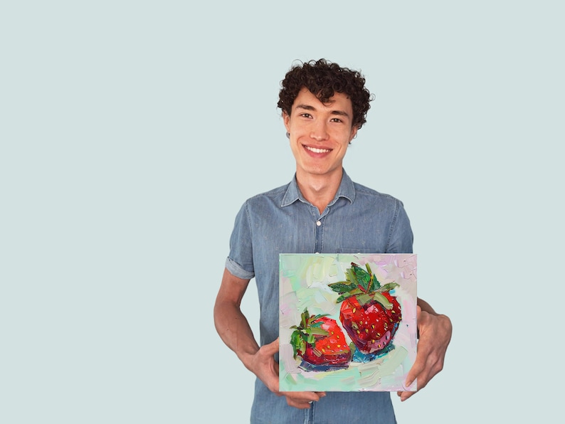 May include: A person holding a painting of two red strawberries with green leaves on a white canvas.