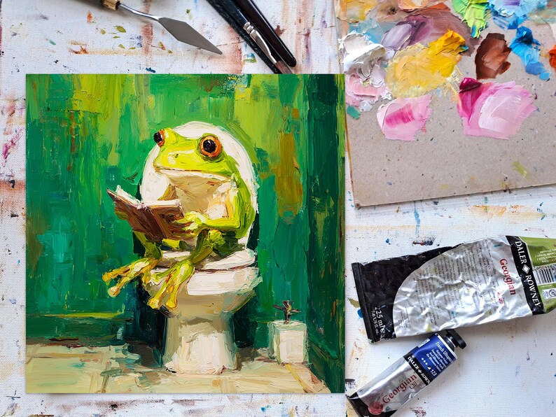 以下が含まれることがあります： トイレで本を読む緑色のカエルの油絵。このアートワークは、緑、黄、茶色のパレットを使用しています。絵の具チューブとパレットナイフが見え、アーティストのスタジオ環境を示唆しています。