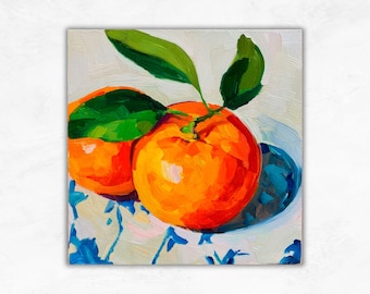 May include: Oil painting of two bright orange tangerines with green leaves, resting in a white bowl with blue floral patterns. The artwork has a textured, impressionistic style, with visible brushstrokes.
