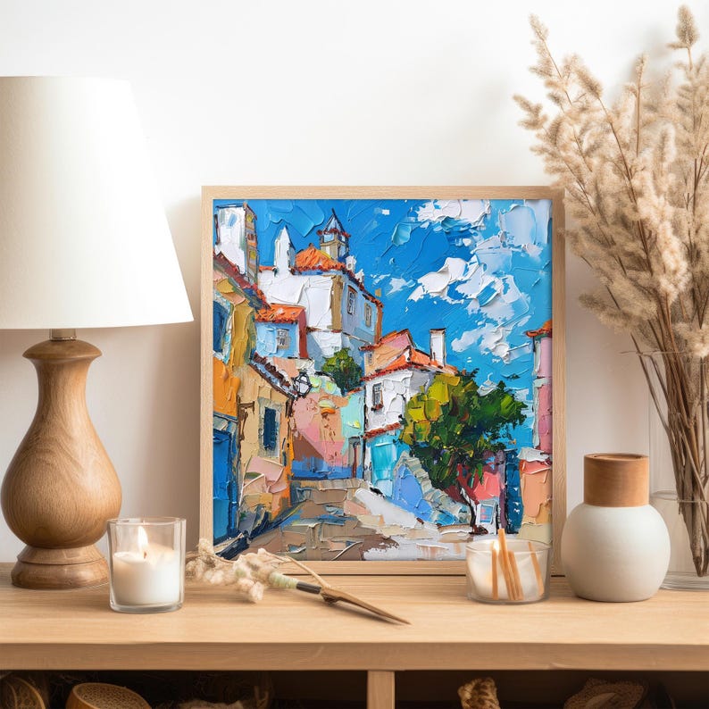 May include: A painting of a colorful, narrow street in a European city. The buildings are painted in shades of yellow, orange, pink, and blue. The sky is a bright blue with fluffy white clouds. The street is cobblestone and there are trees and plants growing along the sides.