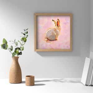 May include: A framed painting of a white rabbit with pink ears sitting on a pink background.
