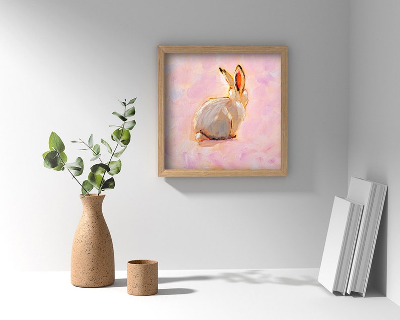 May include: A framed painting of a white rabbit with pink ears sitting on a pink background.