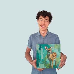 Puede incluir: Arte en lienzo cuadrado con un ciervo sobre un fondo abstracto turquesa y verde. El ciervo est&aacute; pintado en tonos marrones y blancos. La obra de arte la sostiene una persona con una camisa vaquera azul.