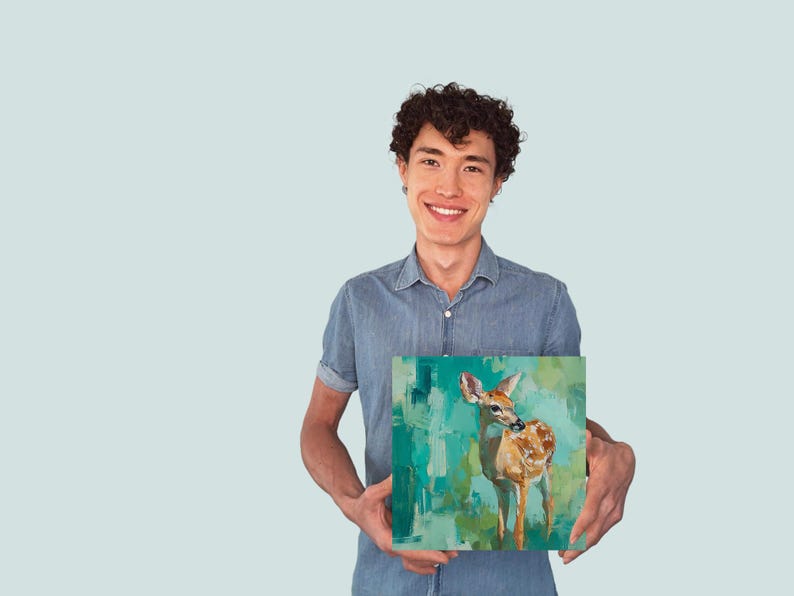 Puede incluir: Arte en lienzo cuadrado con un ciervo sobre un fondo abstracto turquesa y verde. El ciervo est&aacute; pintado en tonos marrones y blancos. La obra de arte la sostiene una persona con una camisa vaquera azul.