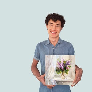 May include: A man in a blue shirt is holding a painting of a vase of purple flowers in front of a window with white curtains.