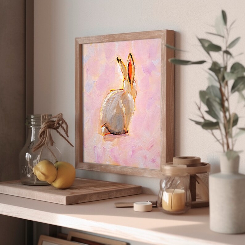 May include: A framed painting of a white rabbit with pink ears against a pink background. The rabbit is facing away from the viewer and has its head tilted slightly to the side.