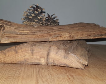 Può includere: Due pezzi di legno rustico impilati l'uno sull'altro. Il pezzo di legno superiore ha due pigne sopra.