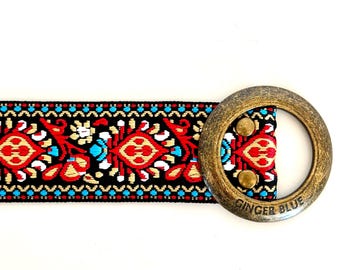 May include: A black and red woven belt with a gold-toned round buckle. The buckle has the words "Ginger Blue" engraved on it.