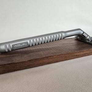 May include: A silver Gillette razor with a textured handle on a dark brown wooden surface.