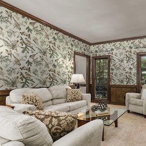 May include: A living room with beige carpet, two white sofas, a glass coffee table, and a brown armchair. The walls are covered in wallpaper with a pattern of birds and branches.