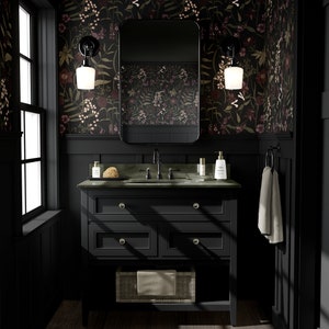 May include: A black bathroom vanity with a dark green countertop and a white porcelain sink. The vanity has three drawers and a lower shelf. The walls are covered in dark floral wallpaper with a black mirror above the sink. Two black sconces with white glass shades are mounted on the wall.