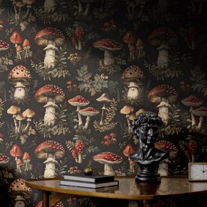 May include: Black and white wallpaper with a repeating pattern of red and white mushrooms and green foliage. A black bust of a man and a clock are on a wooden table in front of the wallpaper.