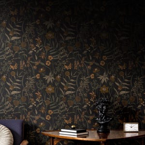 May include: A dark floral wallpaper with a black and gold pattern. The wallpaper features a variety of flowers and leaves, including lilies, roses, and ferns. The wallpaper is shown in a room with a wooden table and a bust of a man.