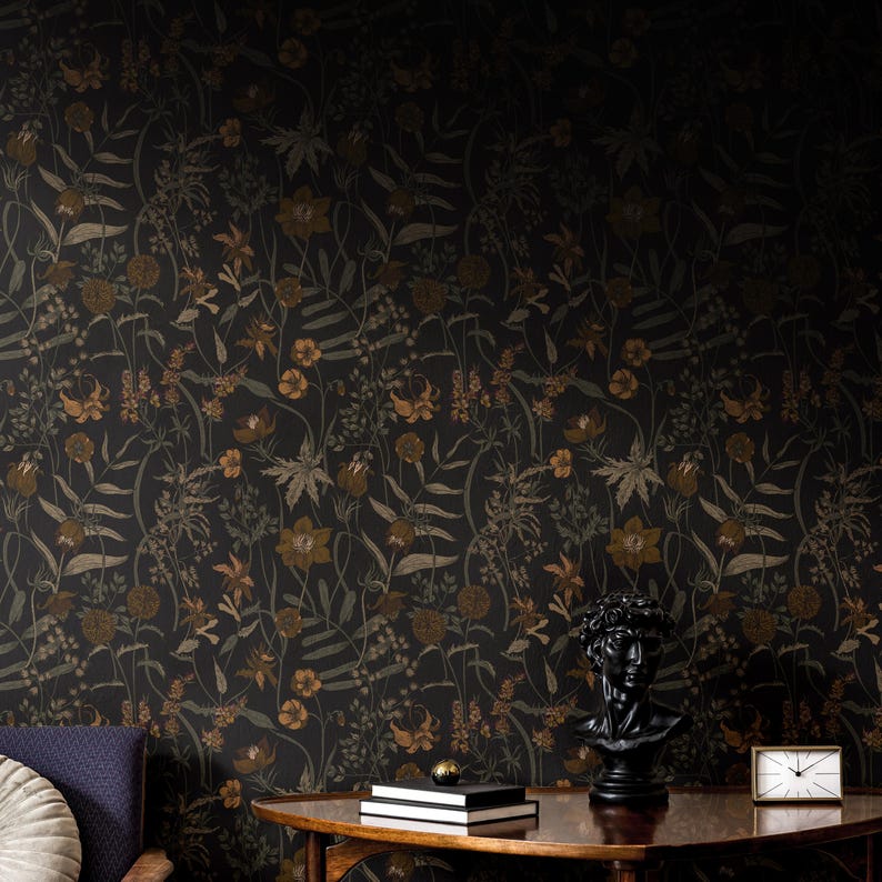 May include: A dark floral wallpaper with a black and gold pattern. The wallpaper features a variety of flowers and leaves, including lilies, roses, and ferns. The wallpaper is shown in a room with a wooden table and a bust of a man.