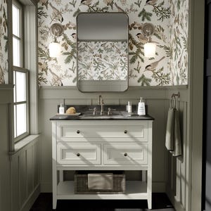 May include: A white bathroom vanity with three drawers and a lower shelf. The vanity has a black countertop with a white porcelain sink and chrome faucets. The vanity is in front of a wall with green wallpaper featuring a repeating pattern of birds and pine branches. The wallpaper has the text "ComfyNoodles" printed on it.